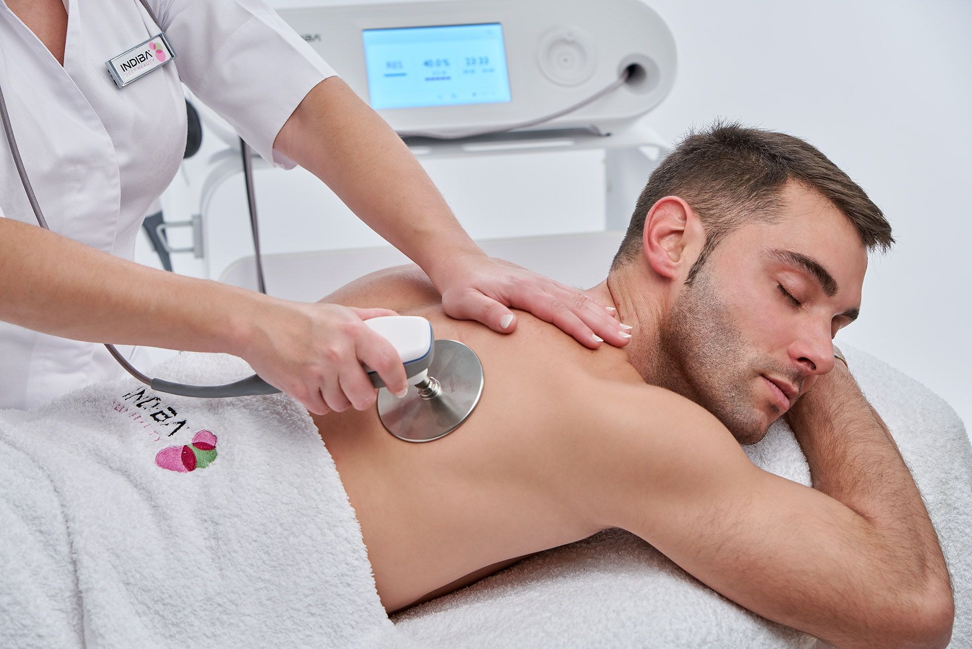 Therapist using device on man's back in a spa setting.