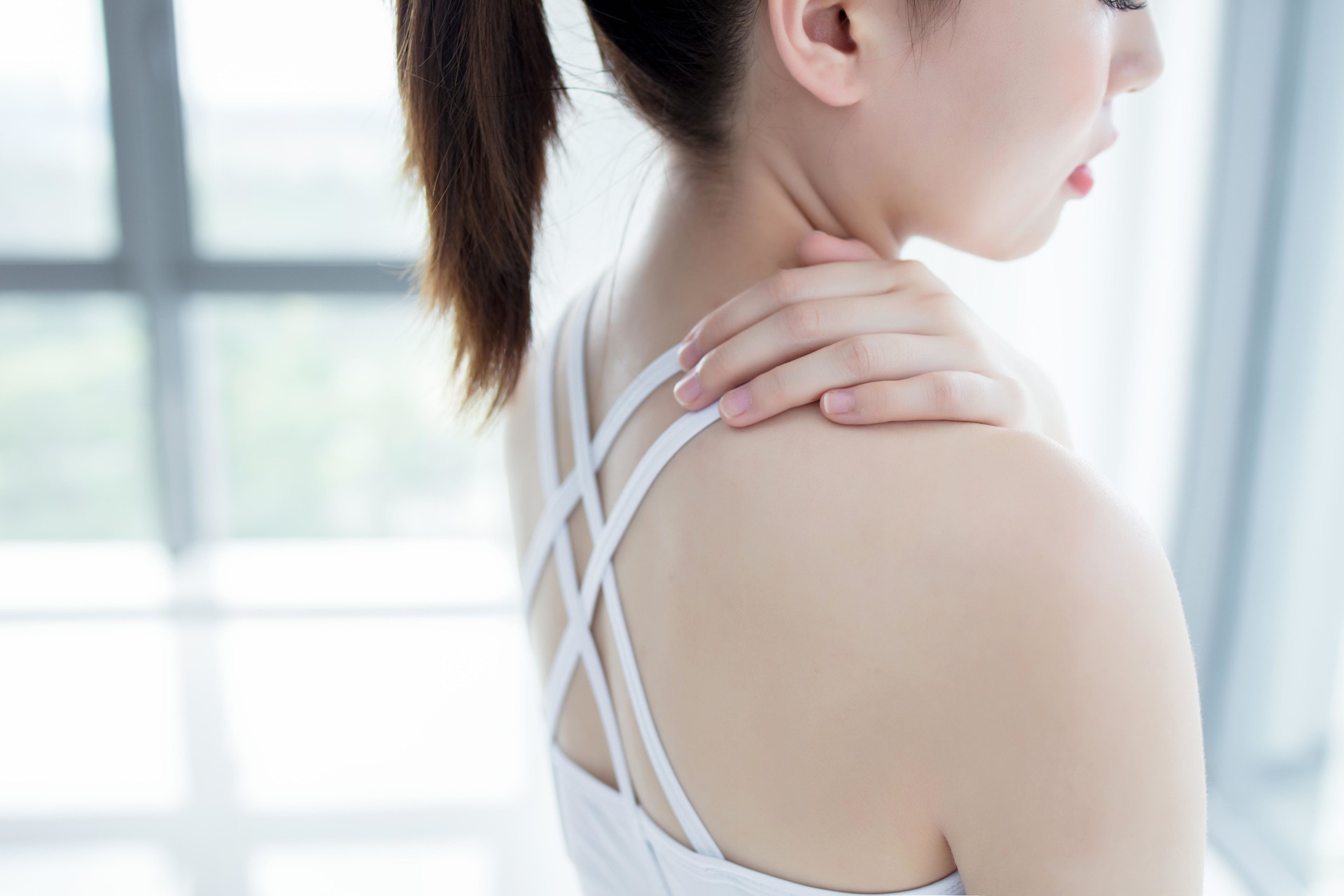 Asian woman in sportswear touching her painful shoulder