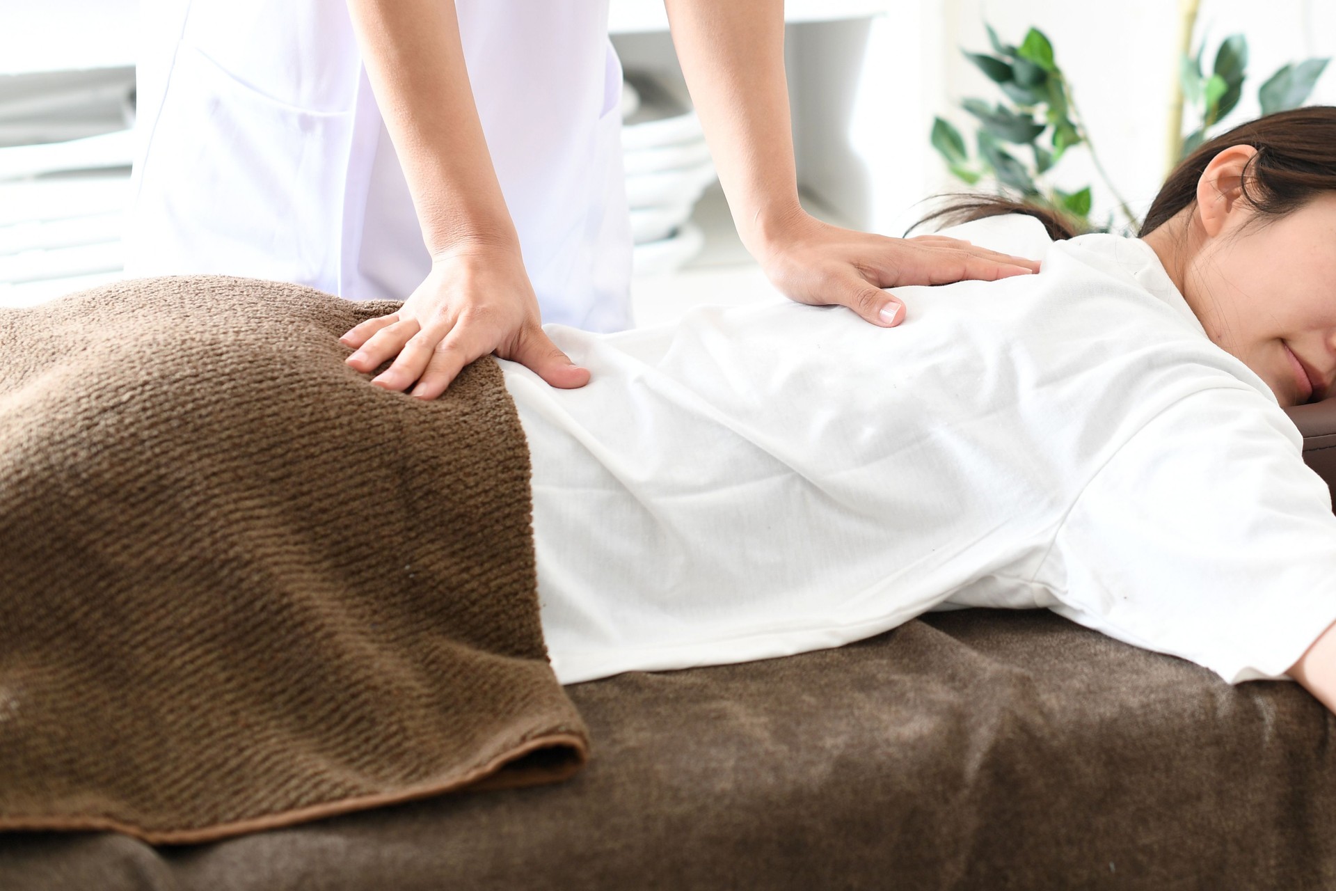 A young Asian woman lying face down receiving massage (manipulative) treatment in bed